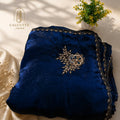 A folded navy blue velvet garment with ornate gold and silver embroidery, displayed on a cream satin fabric with decorative dried flowers and a small potted plant. The brand logo 'CALCUTTA saree' is visible in the top left corner.